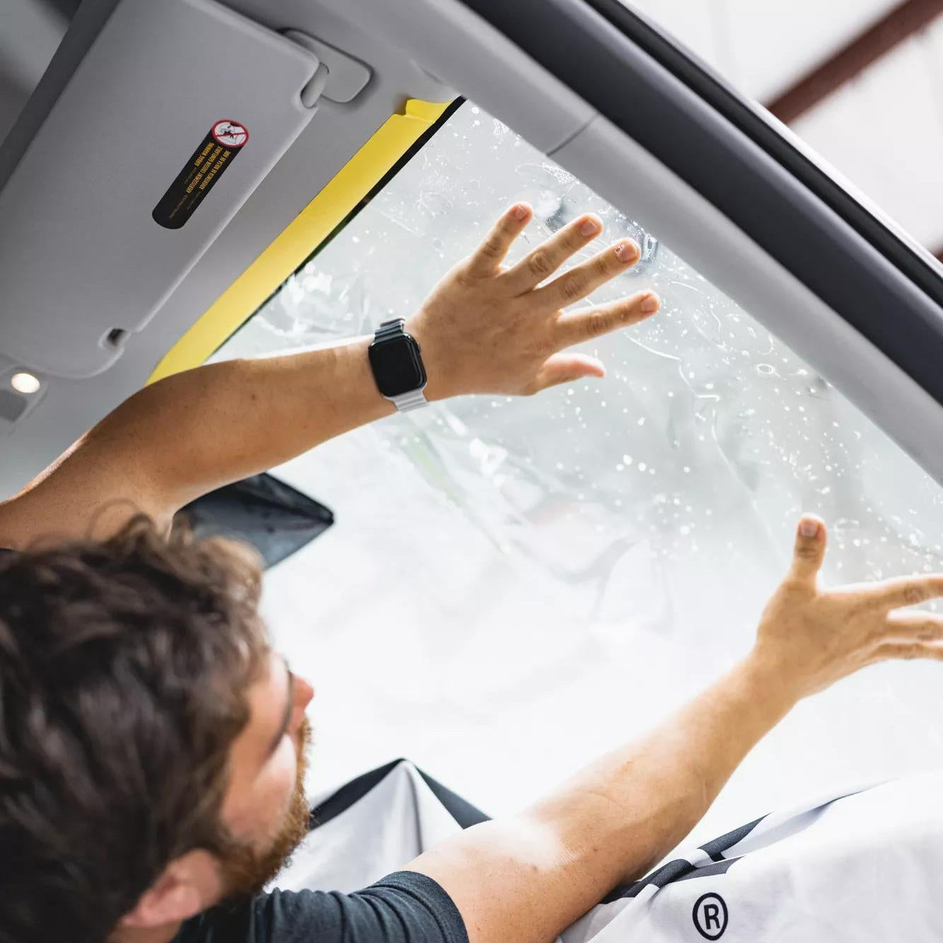 Person installing a car sunshade inside a vehicle