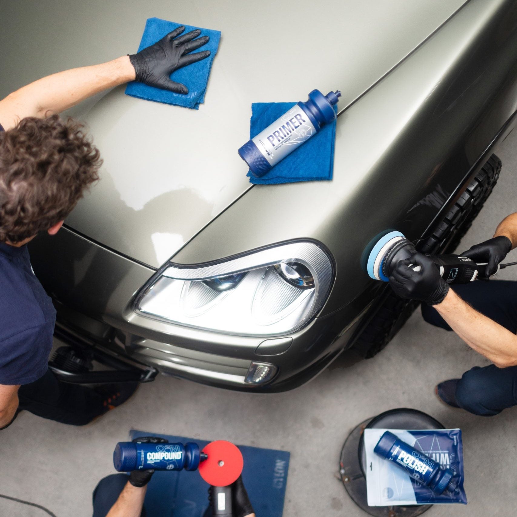 Three people working on a car with a polisher and cleaning supplies in garage in Atlanta Marietta